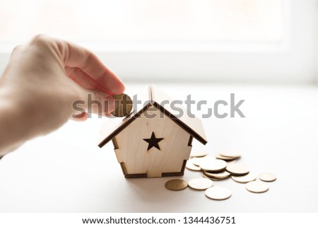Closeup of hand putting coin in wood house piggy bank on white background. place for text. Saving money, home loan, mortgage, a property investment for future concept.