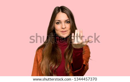 Young woman with coat inviting to come with hand. Happy that you came over isolated pink background