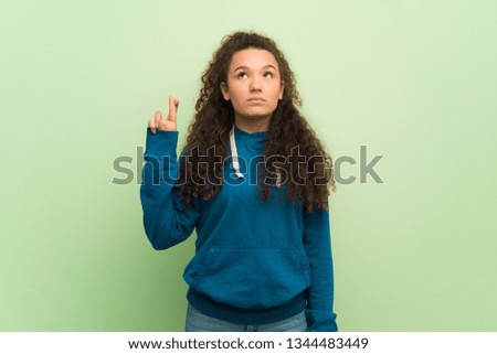 Teenager girl over green wall with fingers crossing and wishing the best