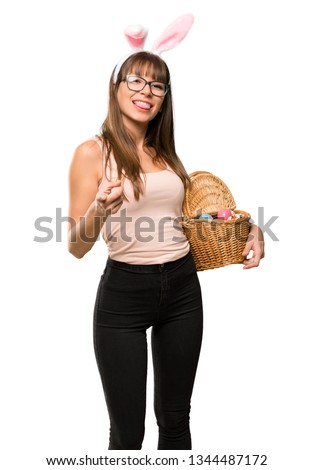 Young woman wearing bunny ears for Easter holidays points finger at you with a confident expression on isolated white background