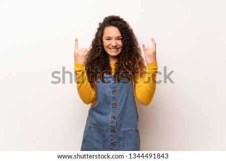 Teenager girl with red sweater over white wall making rock gesture