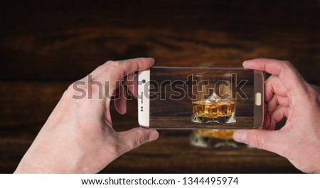 Man taking photo of Whisky or whiskey or bourbon with ice on wood background