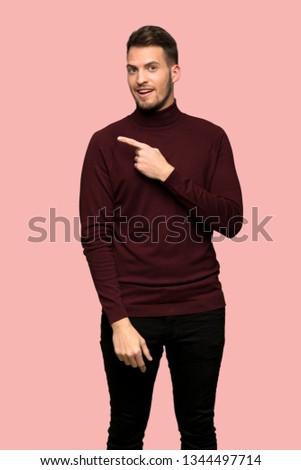 Man with turtleneck sweater pointing to the side to present a product over pink background