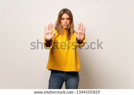 Woman with yellow sweater over isolated wall making stop gesture and disappointed