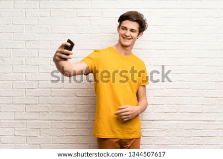 Teenager man over white brick wall making a selfie