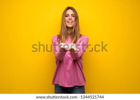 Woman with pink sweater over yellow wall holding copyspace imaginary on the palm to insert an ad