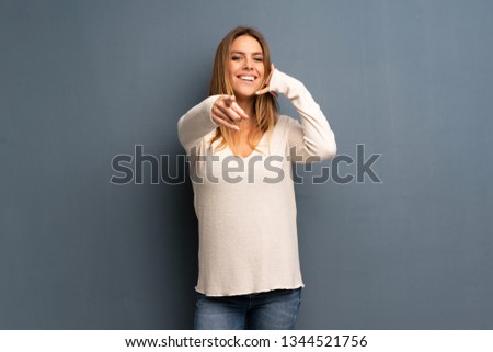 Blonde woman over grey background making phone gesture and pointing front