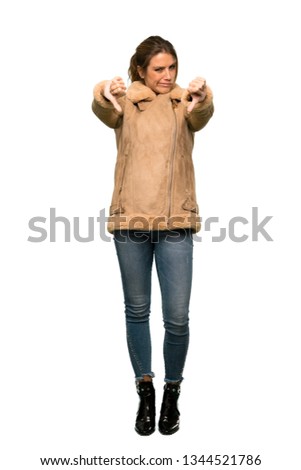 A full-length shot of a Blonde woman with a coat showing thumb down over isolated white background