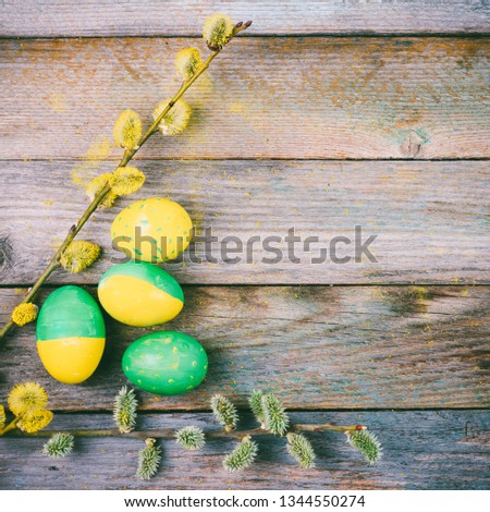 Easter composition of blooming willow twigs and Easter eggs with a pattern of yellow and green color on a wooden retro background with copy space close-up top view