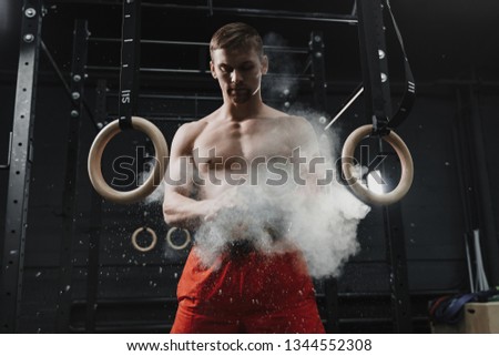 Muscular crossfit athlete clapping hands and preparing for workout at the gym. Cloud of dust chalk powder magnesia protection on dark background. Sport concept.