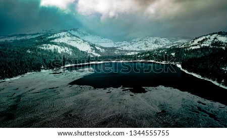 Aerial photo of Donner Lake near Lake Tahoe, frozen over in winter, California, taken with drone, can see storm building in background.  Ice on the surface of the lake, dark and cold and stormy