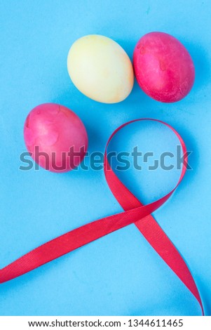 On a blue background Easter composition. Red silk ribbon with colorful easter eggs. Religious holiday. View from above