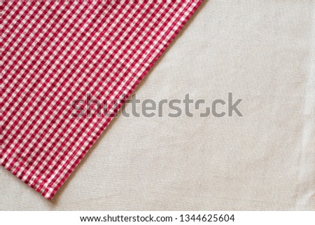 Red and White Checked Cloth at angle on upper corner of off white or cream colored linen table cloth.  Horizontal above view with room or space for copy, text or your words or design