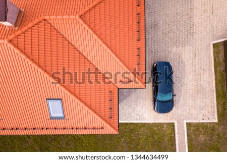 Aerial top view of house metal shingle roof with attic windows and black car on paved yard.