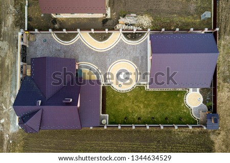 Aerial top view of house shingle roof on background of green lawn and colorful paved yard with geometrical abstract pattern.