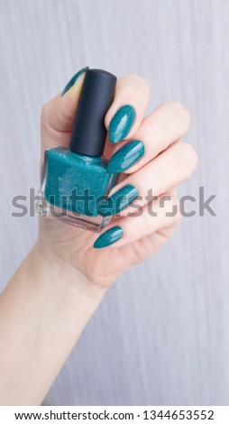 Female hand with Teal turquoise long nails and a bottle of nail polish