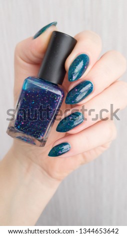 Female hand with Teal turquoise long nails and a bottle of nail polish