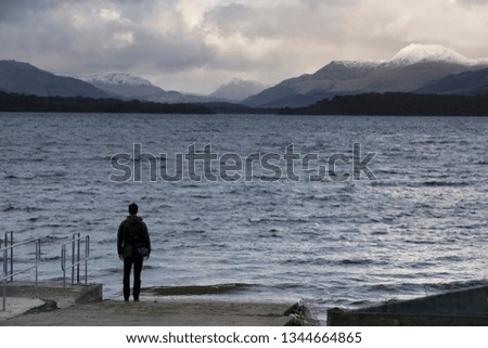 Lonely man in wild landscape mountains and lake in winter storm clouds at Loch Lomond Scotland