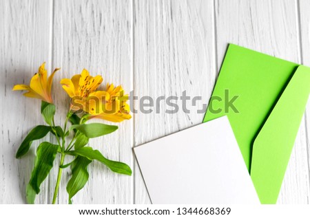 Mock up blank paper and envelope on white wooden background with natural flowers of yellow color. Blank, frame for text. Greeting card design with flowers.