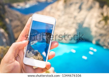 Hand holding mobile phone taking photo of beautiful landscape; Tourist filming video of holiday destination for memory; Summer holiday background with copy space