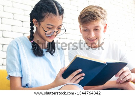 girl and boy witting on sofa and try to looking and reading a book together as learning or group homework concept  