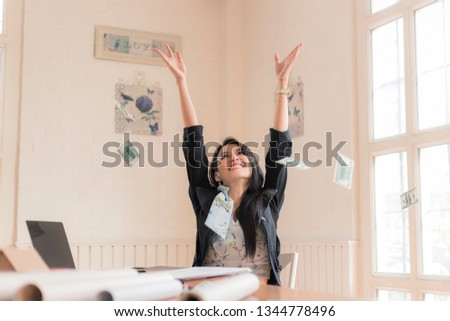  business woman with his hands raised while working on laptop with money rain