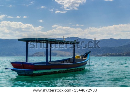 
Ilha Bela - Brazil / Blue, red and white boat, over green sea with blue sky white clouds and mountains and island in background