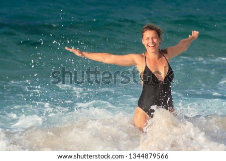 Funny girl in swimsuit is swimming in blue sea water. Woman splashing in sea waves and drops