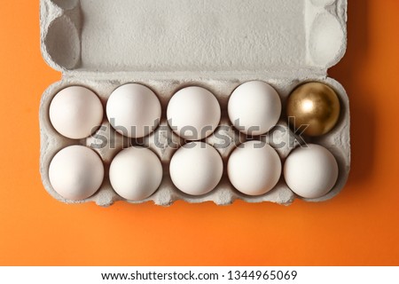 Box with golden egg among white ones on color background. Concept of uniqueness Royalty-Free Stock Photo #1344965069