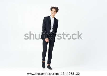 Curly guy in a full-length suit on a light background                       