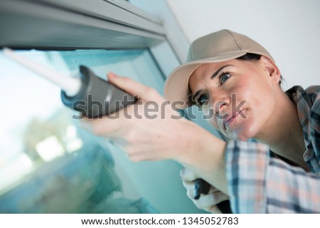 concentrated woman applying silicone to window Royalty-Free Stock Photo #1345052783