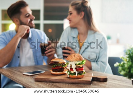 Young couple having lunch in restaurant, focus on board with burgers
