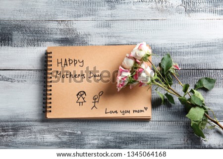 Notebook with greeting for mother and flowers on wooden background