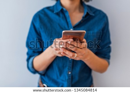 Close-up image of young hipster girl using modern smartphone device, female hands typing text message via cellphone, social networking concept, isolated over gray background