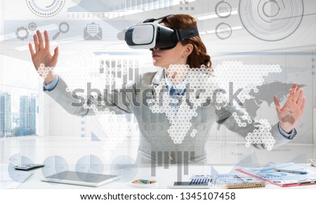 Beautiful and young business woman in suit using virtual reality headset with digital media structure while standing inside bright office. Up to date technologies