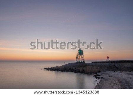 green and red lighthouse of the harbor entrance of Stavoren, Netherlands, photographed at sunset and blue hour from the beach 