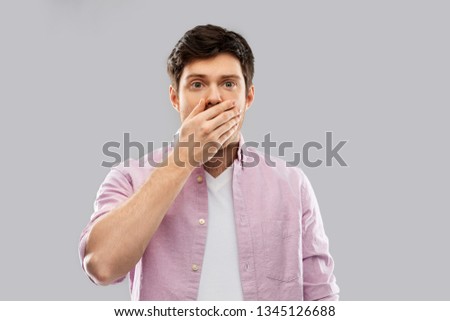 emotion, expression and people concept - shocked and speechless young man covering his mouth by hand over grey background