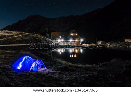 Night mountain landscape with illuminated blue tent. Mountain peaks and the moon. outdoor at Lacul Balea Lake, Transfagarasan, Romania. Concept Travel, copy space