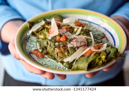 Chef in blue tunic holds spinach pancakes with salmon and parmesan in a creamy sauce on a beautiful plate. close-up. space