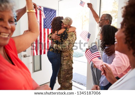 Millennial woman and family welcoming young black male soldier home, embracing in doorway, close up