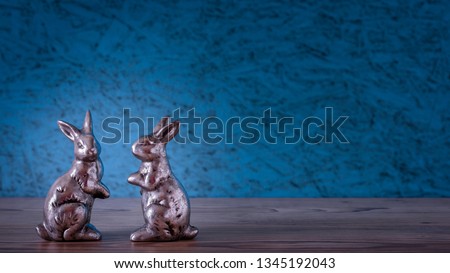 Two silver rabbits in front of a blue background