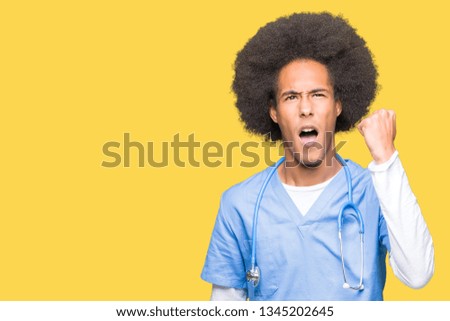 Young african american doctor man with afro hair angry and mad raising fist frustrated and furious while shouting with anger. Rage and aggressive concept.