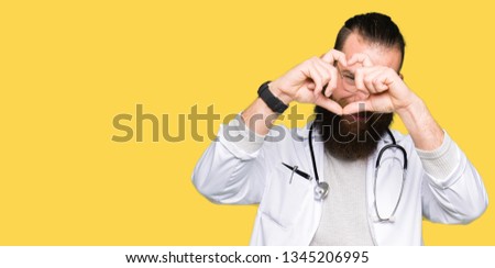 Young blond doctor man with beard wearing medical coat Doing heart shape with hand and fingers smiling looking through sign