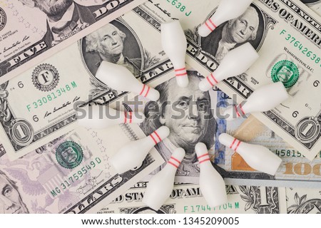 Financial success target concept, red winning bowling strike ball surround with knocked down pins on pile of US dollar banknotes money, goals on investment or profit in stock market metaphor.