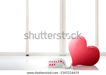Red heart and a white paper tags on the table with Health day message with white window background. Health day concept