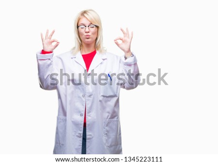 Young beautiful blonde professional woman wearing white coat over isolated background relax and smiling with eyes closed doing meditation gesture with fingers. Yoga concept.