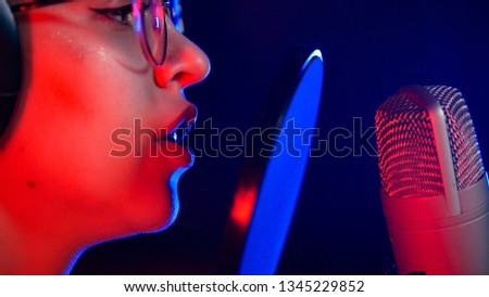 A young woman in glasses singing in neon lighting by the microphone