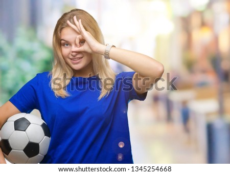 Young caucasian woman holding soccer ball over isolated background with happy face smiling doing ok sign with hand on eye looking through fingers