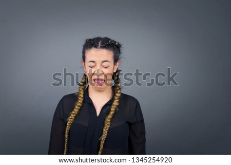 Body language. Disgusted stressed out pretty girl with braided hair and braces on teeth posing against gray wall, frowning her face, closing eyes demonstrating aversion to something.
