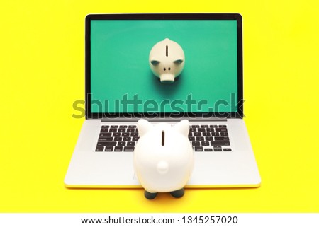 Small piggy bank standing on notebook and looking to laptop monitor, isolated on yellow background, on the computer screen picture with piggy bank on green background 